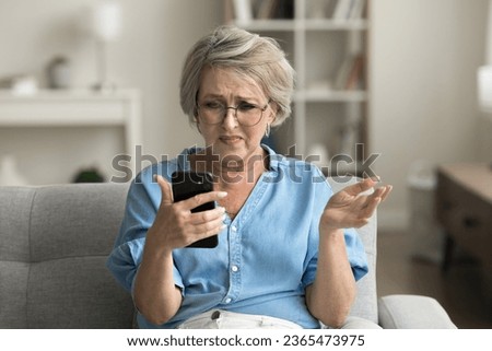 Annoyed frustrated mature retired woman in glasses getting problems with smartphone, trouble with online connection, communication, reading bad news, using mobile phone Royalty-Free Stock Photo #2365473975