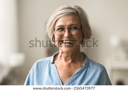 Cheerful pretty blonde older woman in elegant glasses looking at camera with beautiful toothy smile, laughing , showing white perfect teeth, posing for elderly female head shot portrait
