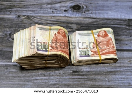 Folded Egyptian money isolated on wooden background, 200 LE two hundred Egyptian pounds cash money bills folded up with rubber bands with a image of the seated scribe on the banknote, selective focus