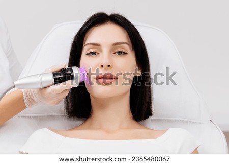 A young woman undergoes a radiofrequency facelift procedure. Advertising concept for facial skin care, anti-aging facial rejuvenation. Radio wave face lifting in a cosmetology clinic. Royalty-Free Stock Photo #2365480067