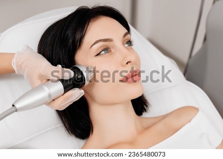 Attractive young woman undergoing a cosmetic procedure in a beauty salon. A woman undergoes fractional RF lifting against a light background. Advertising concept for clean and young facial skin. Royalty-Free Stock Photo #2365480073