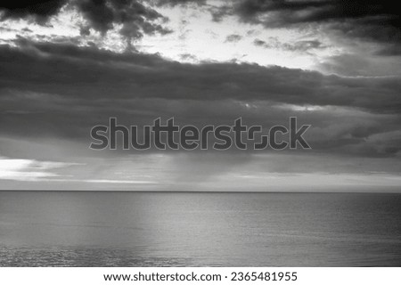 Cloudy sky over the horizon of a sea bay at sunset, black and white
