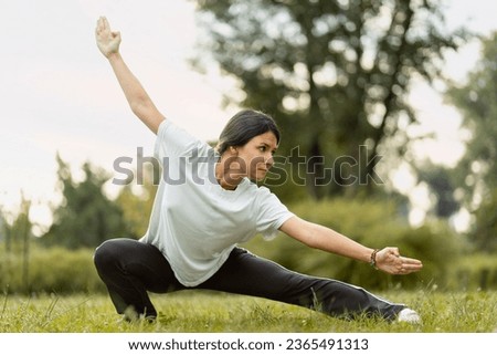Portrait of serious woman wearing sport clothes training, practicing wushu in park. Healthy lifestyle, kungfu, martial arts concept Royalty-Free Stock Photo #2365491313