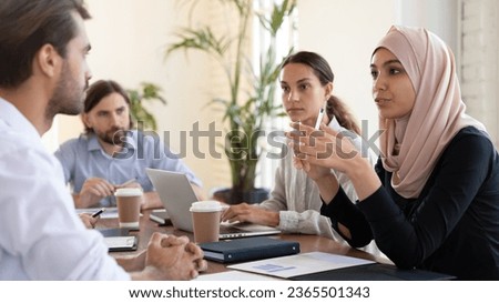 Multicultural businesspeople negotiating gathered together at office group meeting led by businesswoman middle eastern ethnicity leader in hijab, talking expressing opinion speak with european partner Royalty-Free Stock Photo #2365501343