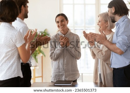 Best employee of month promoted successful female worker or newcomer receiving appreciation or encouragement from diverse staff clap hands her while she folded arms over chest feels flattered grateful Royalty-Free Stock Photo #2365501373