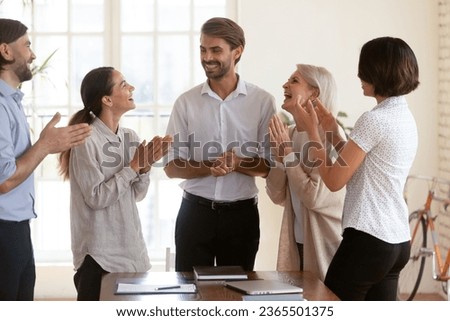 Five diverse businesspeople standing in boardroom clap hands congratulating team leader, best employee of month receiving admiration from young and aged colleagues. Achievement success at work concept Royalty-Free Stock Photo #2365501375