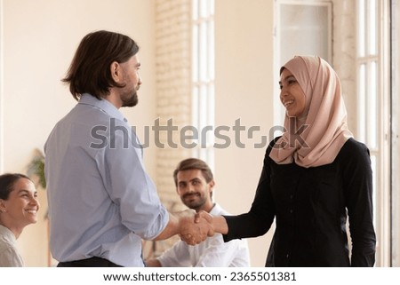 Middle eastern ethnicity Arabian female in hijab worker shake hands with boss receiving praises and gratitude for good work done. Accomplishing seminar express appreciation to business trainer concept Royalty-Free Stock Photo #2365501381