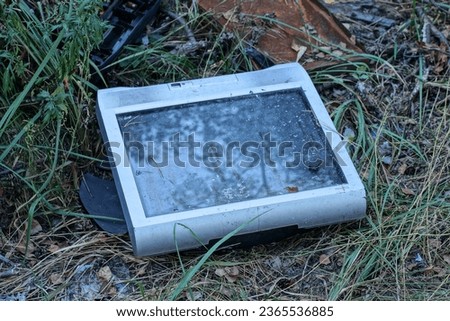 garbage from one old gray square TV lies on the ground and in the green grass on the street