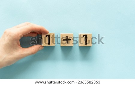 1 and 1 inscription on wooden cubes and a hand holding a cube on a blue background