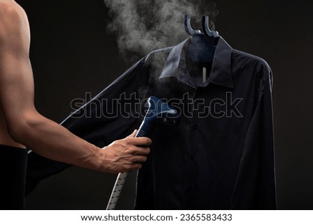 A man irons a dark shirt with a steamer on a black background.