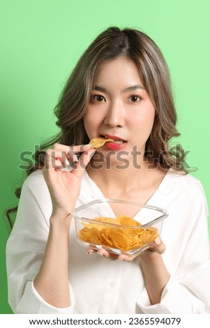 The Asian woman eating potato chips from the hand on the green background. Royalty-Free Stock Photo #2365594079