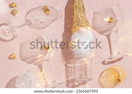 Happy New Year and Christmas holiday flat lay pattern, sparkling wine champagne bottle and wine glasses, xmas glass transparent balls on pink background. Cute dwarf in sequins hat as bottle decor