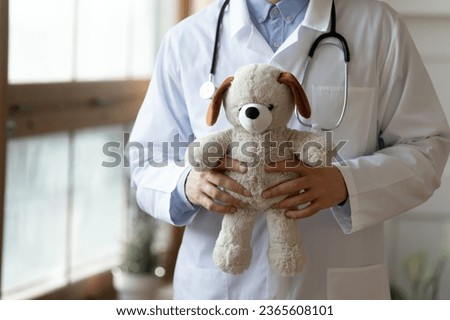 Close up male pediatrician wearing white coat uniform with stethoscope holding fluffy toy, gp therapist practitioner standing in modern hospital, children healthcare and health insurance concept Royalty-Free Stock Photo #2365608101