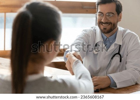 Smiling doctor wearing glasses shaking female patient hand at meeting in hospital, therapist gp greeting woman at medical appointment consultation, counselor advisor making deal with client Royalty-Free Stock Photo #2365608167