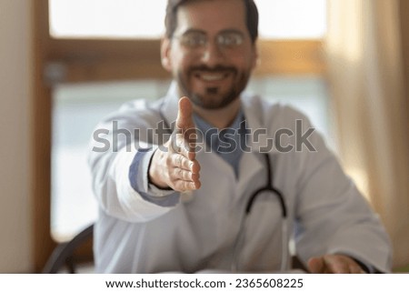 Close up smiling doctor extending hand for handshake to camera, friendly gp therapist wearing white coat uniform with stethoscope greeting patient at medical appointment, acquaintance concept