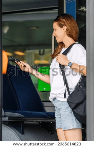 Young woman passenger of public transportation in city paying for trolleybus travel using her mobile phone. Royalty-Free Stock Photo #2365614823