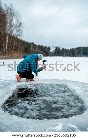 Winter swimming. A woman carving an ice hole entry in lake with axe