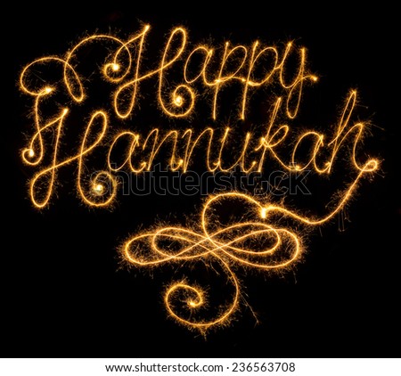 Happy Hannukah greeting in cursive handwriting done with sparklers on black background.