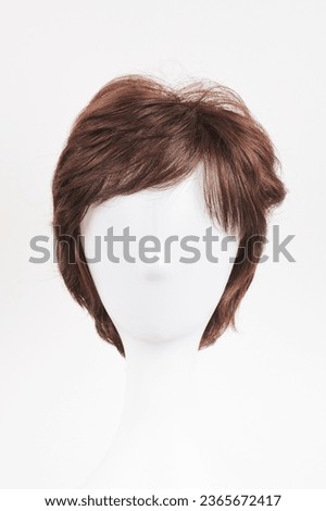 Natural looking dark brunet wig on white mannequin head. Short brown hair on the plastic wig holder isolated on white background, front view  
