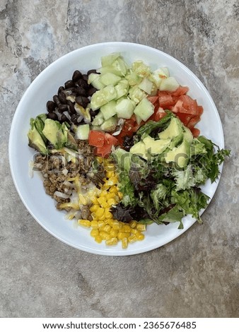 Taco salad nutritional meal of black beans, greens, tomatoes, cucumber, mindful cheese, avocado, ground cooked turkey with taco seasoning and corn