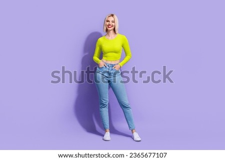 Full size photo of good mood girl wear stylish yellow shirt denim pants standing hold arms in pockets isolated on violet color background