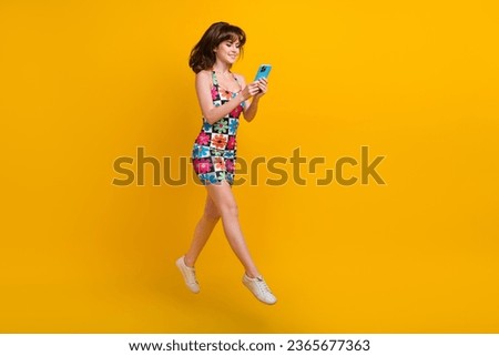 Full length photo of shiny pretty lady wear flower print clothes jumping high communicating gadget isolated yellow color background