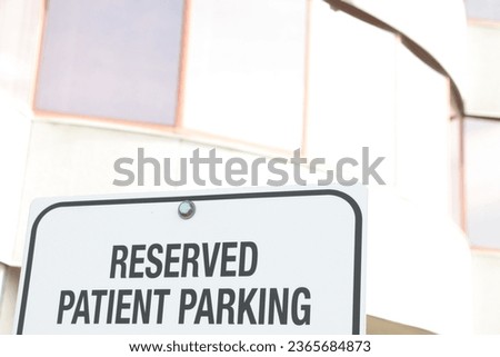 reserved patient parking writing caption text words sign with bright office building behind in sunshine, black writing on white background
