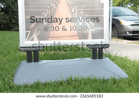 sunday services 830 and 1030 time sign information on grass lawn next to sidewalk and street road in summer on bright day with car vehicle parked on road street