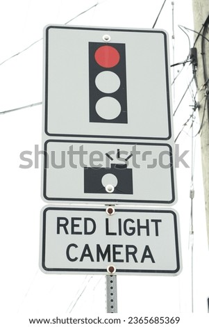 red light camera text sign with three atop each other with illustration of picture camera and red traffic light on metal post, portrait