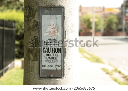warning entry may result in physical injury caution buried cable before digging contact the local hydro sign on cement concrete post with bright sun shining on one side and shade on other, tight shot