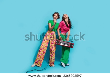 Full size photo of two young funky happy relatives sisters listen boombox karaoke song vocalists isolated on blue color background