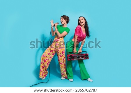 Full body photo of two pretty girlfriends sing microphone favorite melody holding boombox vintage device isolated on blue color background