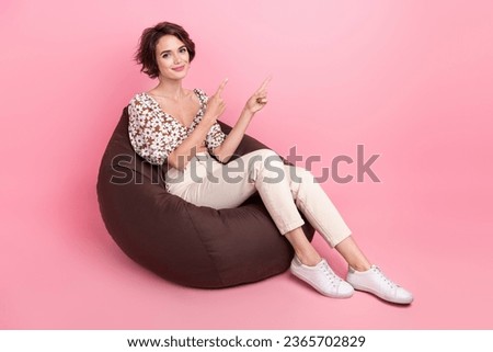 Full length photo of positive woman wear print top sit on bean bag indicainting at sale empty space isolated on pink color background