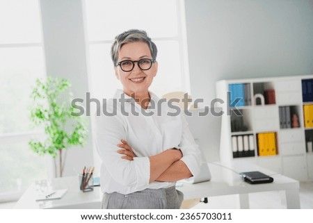 Photo of confident positive lady employer dressed white shirt eyewear arms folded smiling indoors workstation workshop
