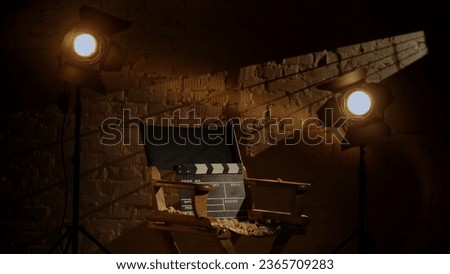 Closeup studio shot of clapperboard standing on director's chair, projectors at the background, popcorn scattered around. Royalty-Free Stock Photo #2365709283