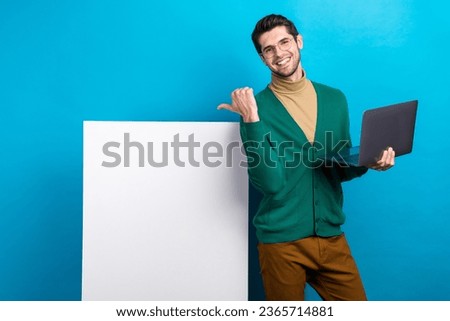 Photo of attractive young man owner company pointing finger banner holding laptop discount for users isolated on blue color background