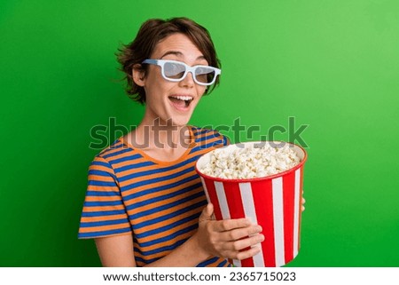 Photo portrait of attractive young woman hold popcorn bucket eating wear trendy striped clothes isolated on green color background