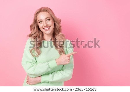 Portrait of interested young woman blonde wavy hair wearing green pullover pointing finger novelty info isolated on pink color background