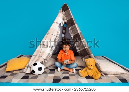 Photo of funny cute boy using smart gadget chatting with friends in tepee isolated blue color background