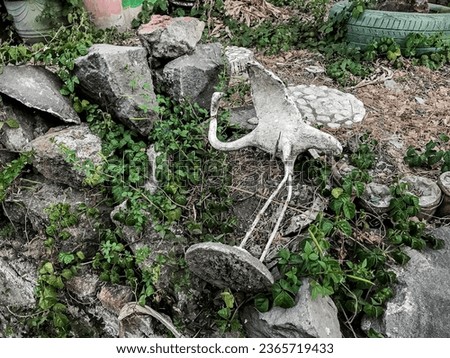 a statue of a fallen crane in the park. architecture, outdoor, garden, historical, art, furniture, grass, bush, island, symbol, outside, broken, old stuff, not maintained, dirty, design, sculpture