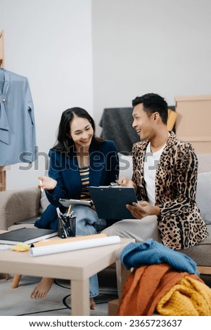 Couple of fashion designers working with fabric and clothing sketches at the studio full of tailoring tools and holds tablet and laptop.  in studio