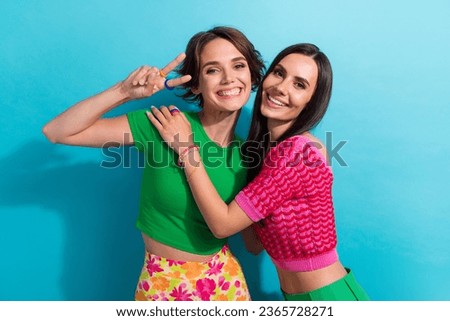 Photo of cute cheerful ladies wear colorful clothes embracing showing v-sign isolated blue color background
