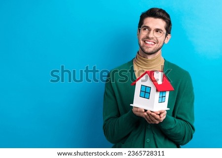 Photo of cheerful minded real estate agent arms hold little house look empty space ad isolated on blue color background