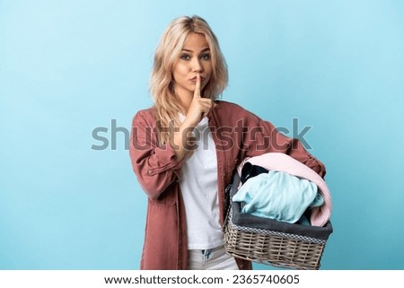 Young Russian woman holding a clothes basket isolated on blue background showing a sign of silence gesture putting finger in mouth