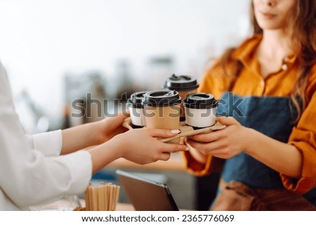 Close-up of a female barista's hands giving out a to-go drink order. The coffee shop owner gives orders to go. Takeaway drinks concept, small business. Royalty-Free Stock Photo #2365776069