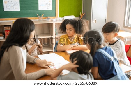 Group of Multi-ethnic elementary school and Female Asian teacher sitting on chairs in circle around and listen to her tell stories in classroom. Education, elementary school, Back to school concept Royalty-Free Stock Photo #2365786389