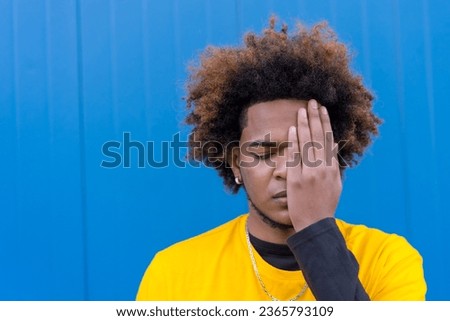 Horizontal photo with blue background of a mixed raced man covering one closed eye
