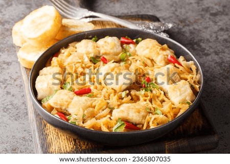 Stewed white cabbage with sea fish fillet, onion and chili pepper close-up in a plate served with toast on the table. horizontal
