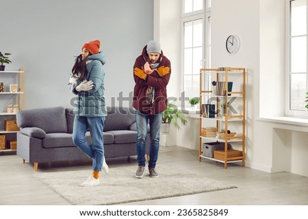 Sad shivering people in winter jackets freezing in cold apartment. Sad warmly dressed young man and woman feeling cold at home on winter season. Central heating problems concept Royalty-Free Stock Photo #2365825849