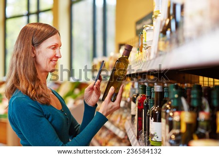 Smiling woman scanning a bottle of olive oil in a supermarket with her smartphone